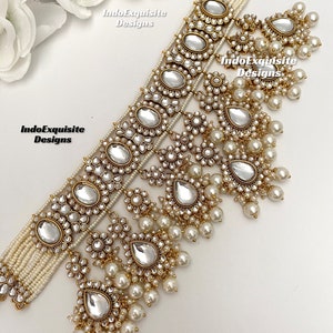 May include: A gold and white layered necklace with pearl accents and a teardrop-shaped pendant. The necklace is decorated with small, clear stones and has a delicate, feminine design. "IndoExquisite Designs" is written on the image.
