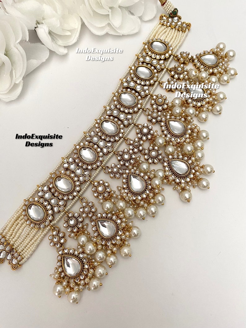 May include: A gold and white layered necklace with pearl accents and a teardrop-shaped pendant. The necklace is decorated with small, clear stones and has a delicate, feminine design. "IndoExquisite Designs" is written on the image.