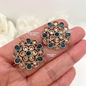 May include: A pair of gold-tone earrings with a circular design. The earrings are adorned with teal blue and white stones.