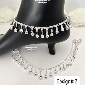 May include: Silver-toned anklet with dangling bell charms. The anklet is displayed on a black foot form, with a second anklet visible below. The text "IndoExquisite Designs" is visible on the image. The design is labeled "Design# 2".