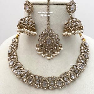 May include: A complete antique gold-toned jewelry set featuring a necklace, earrings, and a headpiece. The necklace and earrings have clear, teardrop-shaped stones and small white pearls. The headpiece is a pendant with a chain.