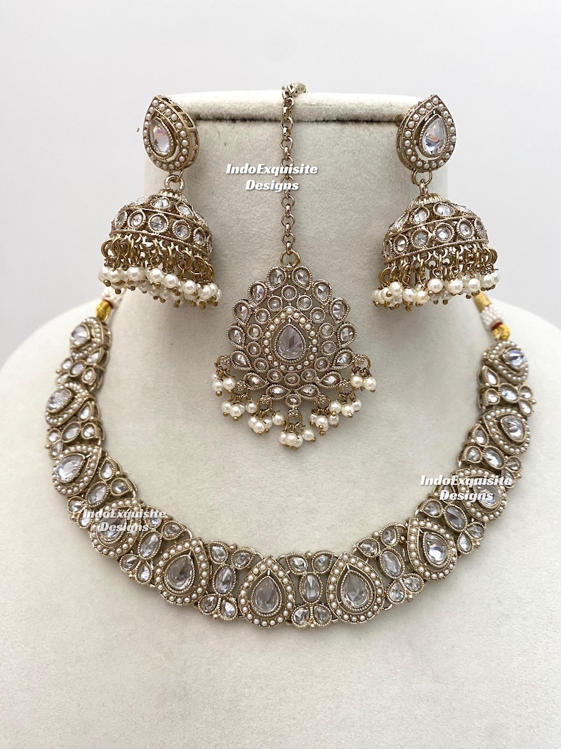 May include: A complete antique gold-toned jewelry set featuring a necklace, earrings, and a headpiece. The necklace and earrings have clear, teardrop-shaped stones and small white pearls. The headpiece is a pendant with a chain.