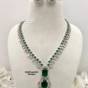 May include: A silver necklace with a green emerald pendant and matching earrings. The necklace features a delicate design with small white stones.