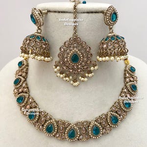 May include: An antique gold-toned jewelry set featuring a necklace, earrings, and a headpiece. The necklace and earrings have teardrop-shaped teal-colored stones. The earrings are bell-shaped with small white pearls. The headpiece has a central teal stone and pearl accents.