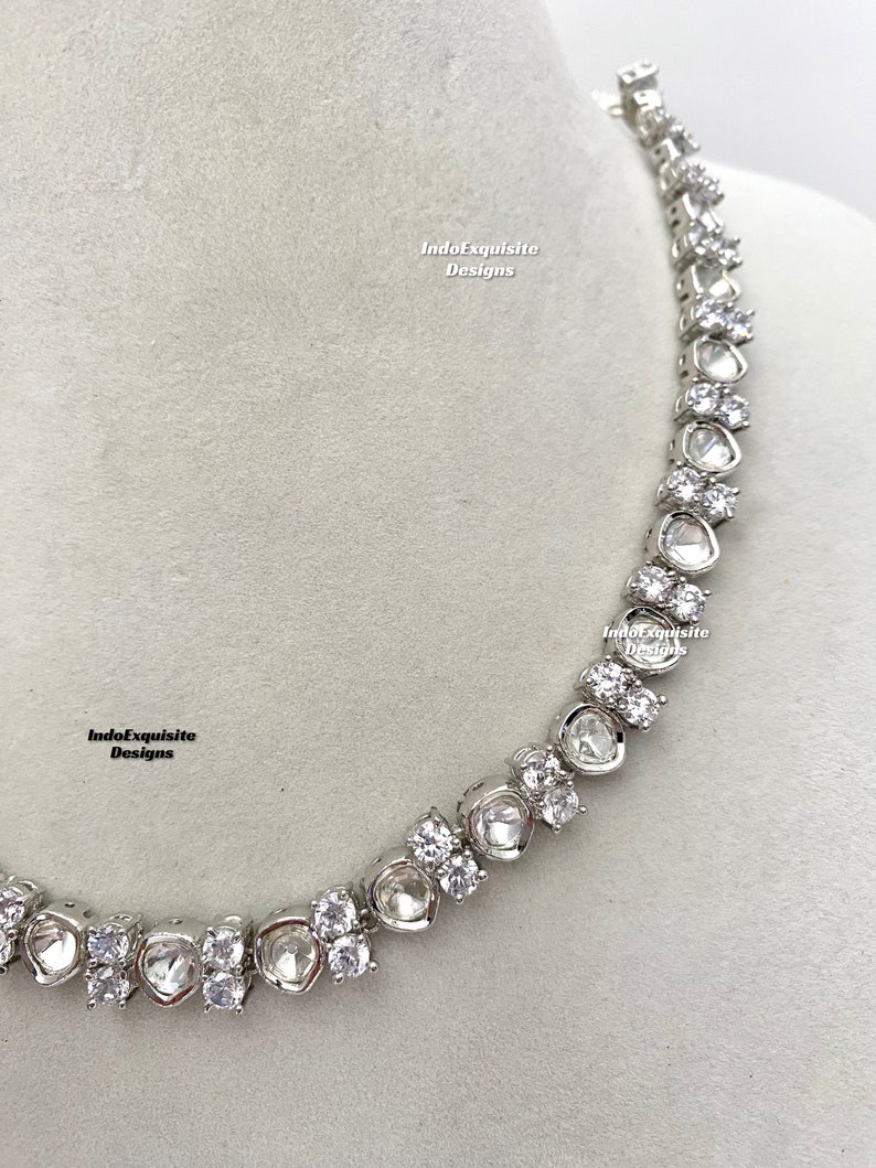 May include: A silver necklace with a row of large, clear, faceted stones. The stones are set in a silver metal setting and are connected by a delicate silver chain. The necklace is a statement piece and would be perfect for a special occasion.