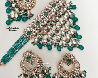 May include: A traditional Indian bridal necklace set with a gold-tone choker, matching earrings, and a maang tikka. The set features a large, ornate pendant with green and white stones, and is accented with green beads.