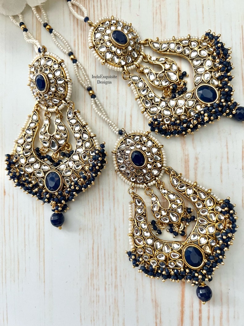 May include: A pair of gold-tone earrings with intricate designs and blue gemstones. The earrings feature a crescent moon shape with a dangling pearl chain.