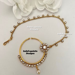 May include: Gold nose ring with a pearl drop and a chain with rhinestones. The chain is attached to the nose ring and has a flower-shaped design with rhinestones.
