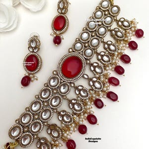 May include: A gold and white choker necklace with red gemstone accents and pearl drops. The necklace is paired with matching earrings.