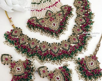 May include: A traditional Indian bridal jewelry set featuring a layered necklace, a matching maang tikka, and earrings. The set is made with gold-toned metal, green and pink beads, and white pearls.