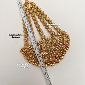 May include: A gold-colored headpiece with intricate floral and beaded designs. The headpiece is measured with a tape measure, showing a length of approximately 5 inches. The text "IndoExquisite Designs" is visible.