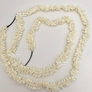 May include: Off-white floral garland with a black cord. The garland is made of small, petal-shaped elements, creating a layered, textured appearance. The design is symmetrical and appears to be handmade.