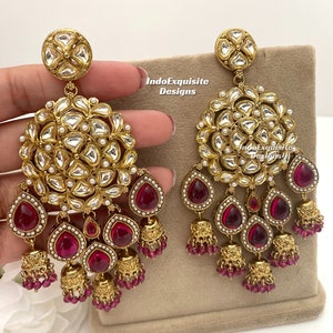 Peut inclure: Une paire de boucles d'oreilles en or avec un motif rond floral et des pierres en forme de larme roses. Les boucles d'oreilles ont plusieurs couches de perles et de clochettes pendantes.