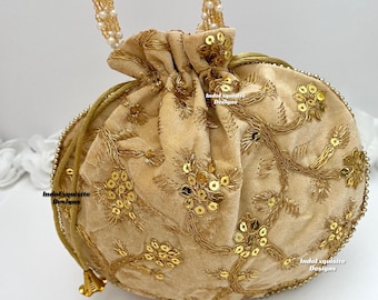 Puede incluir: Una bolsa de cordón de terciopelo beige con bordados y lentejuelas doradas. La bolsa tiene una correa de perlas y cuentas.