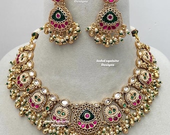 Puede incluir: Un conjunto de collar y pendientes en tono dorado con piedras de color verde oscuro y fucsia, acentuado con pequeñas perlas blancas y cuentas verdes. La joyería muestra un trabajo de metal intrincado y el texto IndoExquisite Designs.