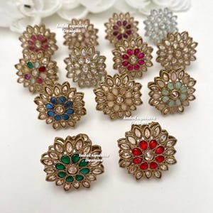 May include: A collection of 12 gold-tone rings with a floral design. Each ring features a different colored gemstone in the center, including red, pink, blue, green, white, and clear.