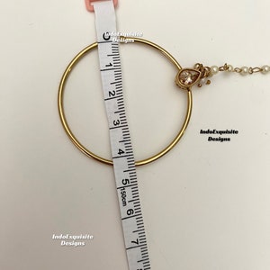 May include: Gold nose ring with a teardrop-shaped crystal and a chain with small white pearls. The ring measures 6 inches in diameter.