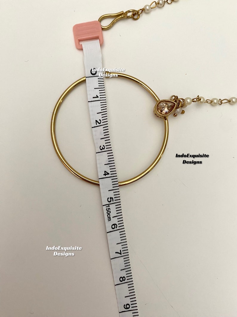 May include: Gold nose ring with a teardrop-shaped crystal and a chain with small white pearls. The ring measures 6 inches in diameter.