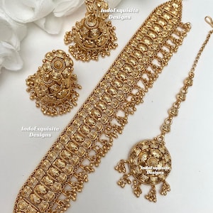 Könnte beinhalten: Ein goldfarbenes Schmuckset mit einer Halskette, Ohrringen und einem Kopfschmuck. Das Set hat ein verziertes, strukturiertes Design mit floralen und geometrischen Mustern. Die Ohrringe sind im Stecker-Stil, und der Kopfschmuck hat einen runden Anhänger.
