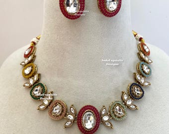 Puede incluir: Un conjunto de joyería que incluye un collar y pendientes ovalados a juego. El collar tiene eslabones ovalados multicolores en rojo, amarillo, verde, melocotón, azul y verde claro, cada uno con una piedra clara en el centro. El texto IndoExquisite Designs es visible.