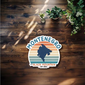 May include: A sticker with a retro design featuring the word "Montenegro" in a circular arc above a dark blue silhouette of the country. Below, the text "The Black Mountain - EST. 2006" is displayed. The background has horizontal stripes in orange, teal, and blue.