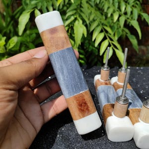 May include: Four marble and wood cabinet knobs with a white, gray, and brown color scheme. The knobs have a square base and a rounded top.
