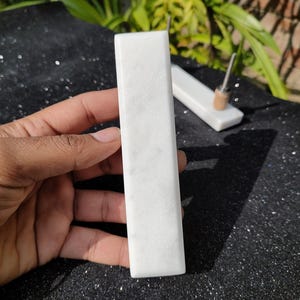 Könnte beinhalten: Zwei rechteckige Blöcke aus weißem Marmor, einer etwas größer als der andere. Der größere Block wird in einer Hand gehalten.