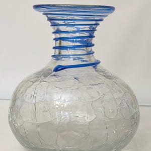 May include: A clear glass vase with a crackled texture and a bulbous body. The neck features a spiral design with blue glass accents. The rim is also trimmed with blue glass. This decorative vase is suitable for home decor.