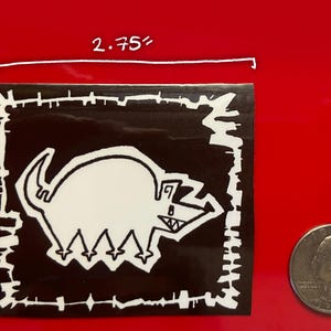 以下が含まれることがあります： 白黒のステッカーに、白い輪郭の漫画の生き物が描かれています。生き物は頭が大きく、体が小さく、各足に3本の指があります。ステッカーのサイズは、7cm x 6.35cmです。