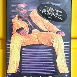 May include: A cassette single by the artist Rome, featuring a photo of the artist in a yellow suit sitting on a chair. The text on the cover reads "Do You Like This" and "The follow up to the smash hit "I Belong To You".