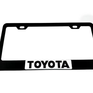 Pu&ograve; includere: Cornice per targa in metallo nero con logo "TOYOTA" bianco.