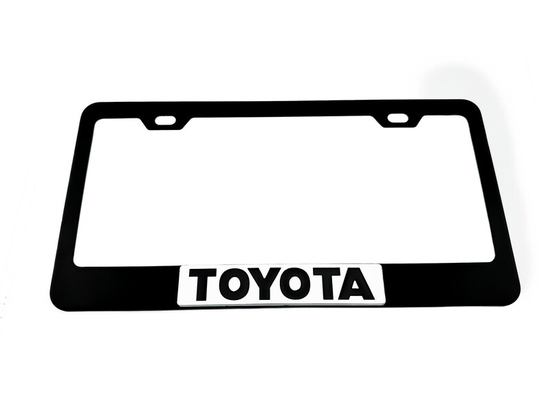 Pu&ograve; includere: Cornice per targa in metallo nero con logo "TOYOTA" bianco.