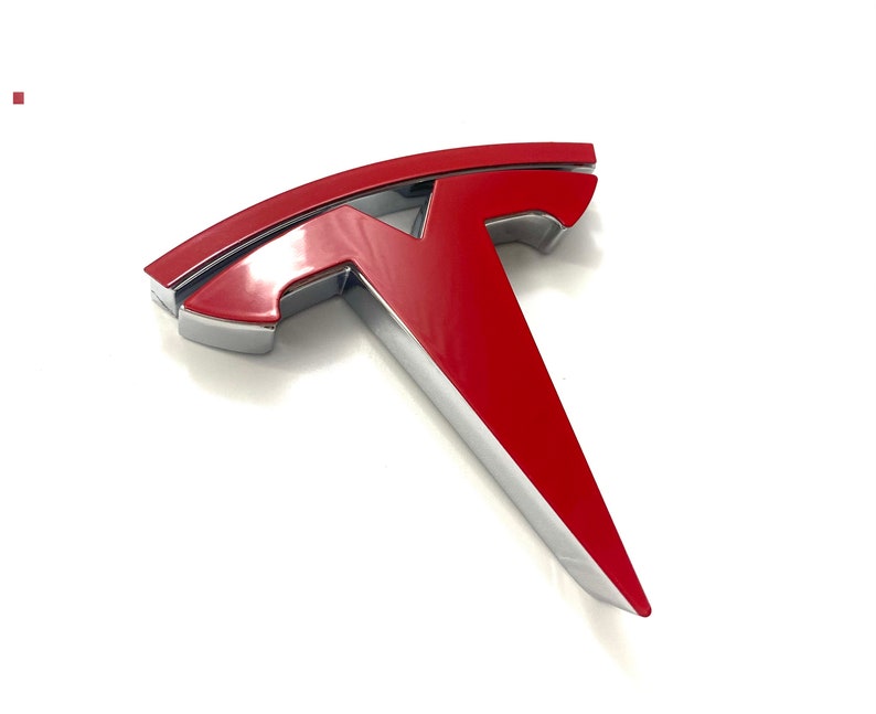 K&ouml;nnte beinhalten: Ein rotes und silbernes Tesla-Logo. Das Logo ist ein stilisiertes T mit einer abgerundeten Oberseite und einer spitzen Unterseite.