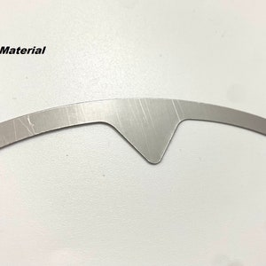 K&ouml;nnte beinhalten: Ein silberfarbenes Metallkernmaterial in Form eines Halbmondes mit einer spitzen Spitze in der Mitte.