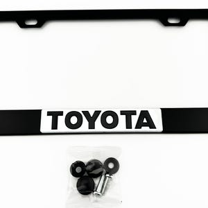 Pu&ograve; includere: Cornice per targa in metallo nero con sfondo argentato e la scritta "TOYOTA" in lettere nere. La cornice viene fornita con quattro viti in plastica nera.