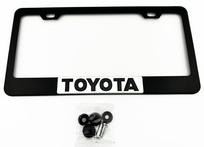 Pu&ograve; includere: Cornice per targa in metallo nero con sfondo argentato e la scritta "TOYOTA" in lettere nere. La cornice viene fornita con quattro viti in plastica nera.