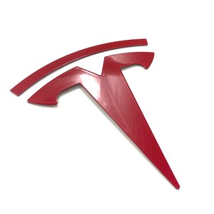 K&ouml;nnte beinhalten: Ein rotes Tesla-Logo aus Metall mit einem stilisierten 'T' und einer geschwungenen Linie dar&uuml;ber.