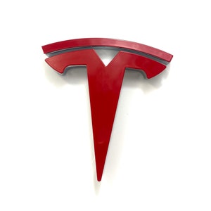 K&ouml;nnte beinhalten: Ein rotes Tesla-Logo mit silbernem Umriss. Das Logo ist ein stilisiertes T mit einer geschwungenen Linie dar&uuml;ber.