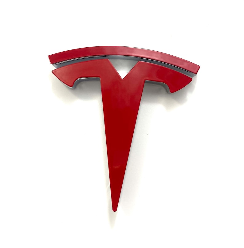 K&ouml;nnte beinhalten: Ein rotes Tesla-Logo mit silbernem Umriss. Das Logo ist ein stilisiertes T mit einer geschwungenen Linie dar&uuml;ber.