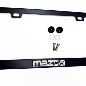 Puede incluir: Marco negro para matr&iacute;cula con el logotipo cromado "Mazda" en la parte inferior. Incluye accesorios de montaje: dos tornillos, dos tapas de tornillo negras y dos arandelas blancas. El marco tiene forma rectangular.