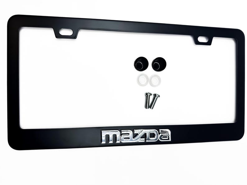 Puede incluir: Marco negro para matr&iacute;cula con el logotipo cromado "Mazda" en la parte inferior. Incluye accesorios de montaje: dos tornillos, dos tapas de tornillo negras y dos arandelas blancas. El marco tiene forma rectangular.