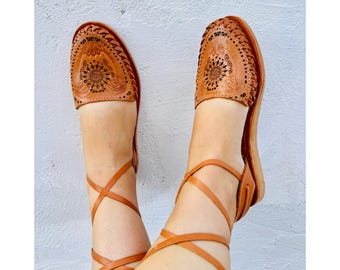 Puede incluir: Sandalias de cuero color canela con intrincados recortes florales y cordones en el tobillo.