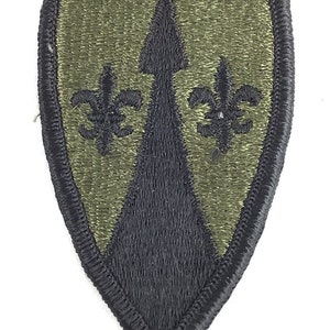 Könnte beinhalten: Ein grünes und schwarzes militärisches Abzeichen mit einem schwarzen Pfeil und zwei schwarzen Fleur-de-lis.