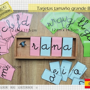 Puede incluir: Un conjunto de tarjetas de letras imprimibles en blanco y negro, con letras cursivas de diferentes tama&ntilde;os. Las tarjetas est&aacute;n impresas en papel rosa, azul y verde. Las tarjetas est&aacute;n dispuestas en una bandeja de madera con una figura de rana. El texto en las tarjetas dice "PDF imprimible", "Tarjetas tama&ntilde;o grande B/N", "wraig ll", "rana", "ch", "ia", "m&sup3;", "12 cm x 11,5 cm", "12 cm x 14,5 cm", "12 cm x 10 cm", "TALLER DE LETRAS".