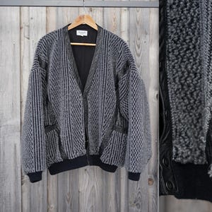 May include: A gray and black striped cardigan with leather accents. The cardigan has a V-neck and a zipper closure.