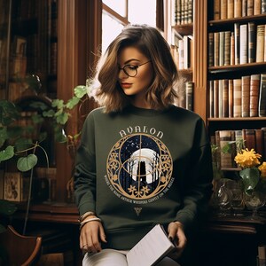 May include: A green sweatshirt with a gold graphic of a moon, trees, and the words "Avalon, Where the Name Arthur Whispers Gently on the Breeze".