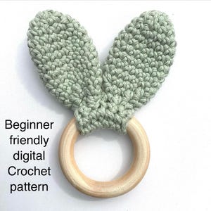 May include: A light green crocheted bunny ear teether attached to a wooden ring. Beginner friendly digital crochet pattern.