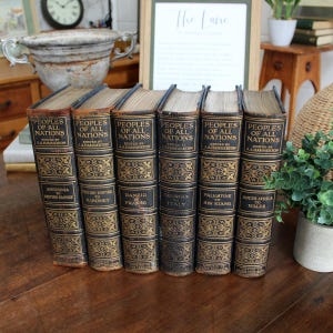 May include: A set of six antique books titled Peoples of All Nations edited by J.A. Hammerton. Each volume features a dark leather spine with gold embossed floral patterns and text indicating the geographical range covered in each specific book.