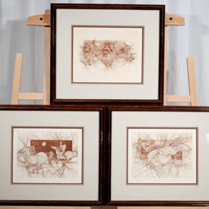 May include: Three framed prints with brown wood frames and white mats. Each print features a black and white line drawing of a horse and rider in a forest setting.