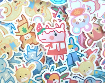 Könnte beinhalten: Eine Sammlung farbenfroher Aufkleber im Cartoon-Stil mit verschiedenen Tierfiguren. Die Aufkleber zeigen eine Vielzahl von Designs, darunter eine rosa Figur mit einer Erdbeere auf dem Kopf, ein blauer Hase und ein gelber Bär. Ideal zum Dekorieren von Notizbüchern, Laptops oder anderen Gegenständen.